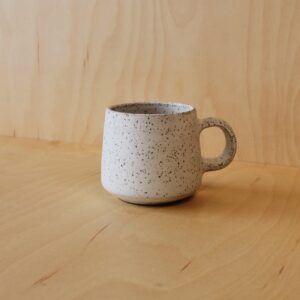 A white speckled mug photographed against a maple wood background.