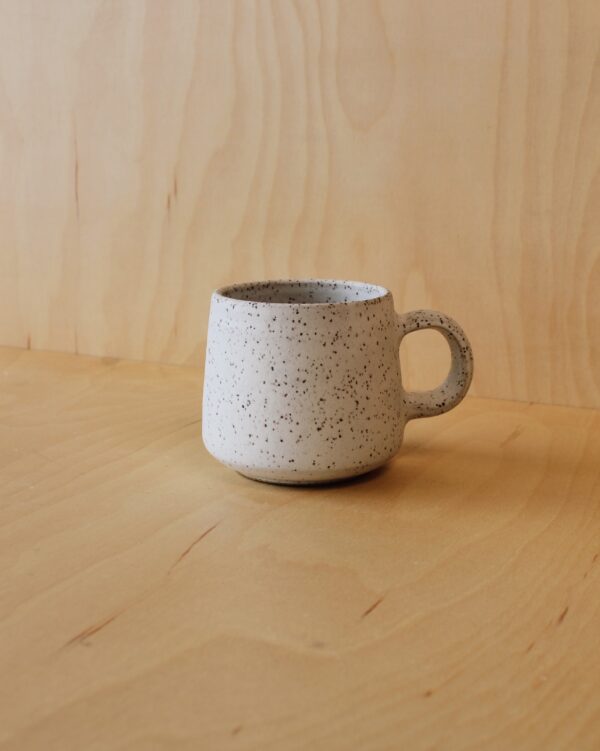 A white speckled mug photographed against a maple wood background.